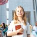 Happy university students socializing on campus, with a focus on a smiling young woman holding a book.